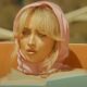 sabrina carpenter wearing head scarf reading book on beach lounger in espresso music video