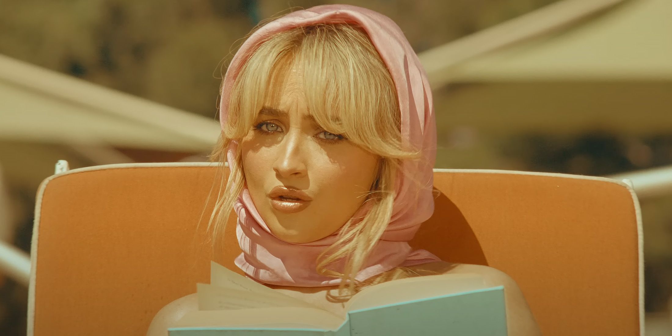 sabrina carpenter wearing head scarf reading book on beach lounger in espresso music video